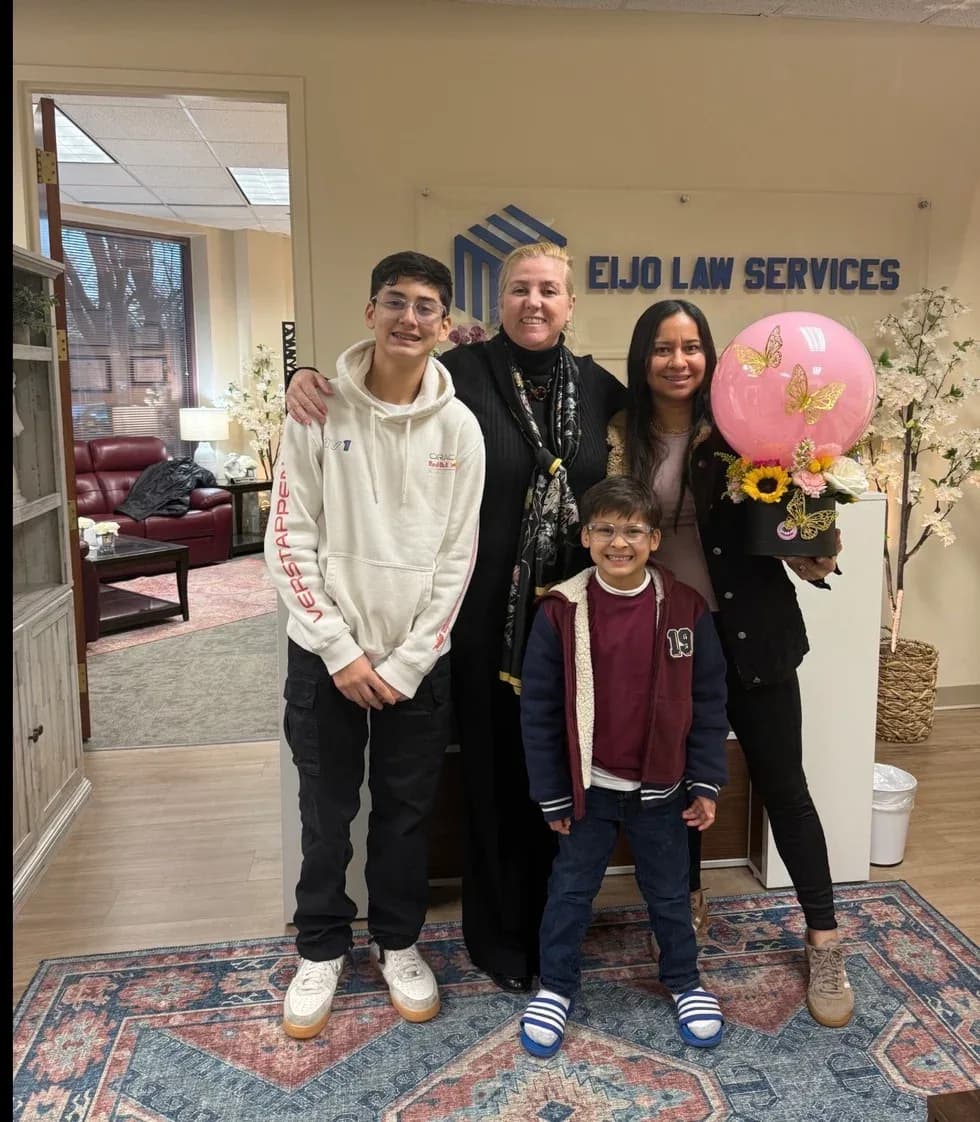 Maria Eijo stands with a woman holding a pink balloon bouquet and flowers, and two boys, in the office lobby.