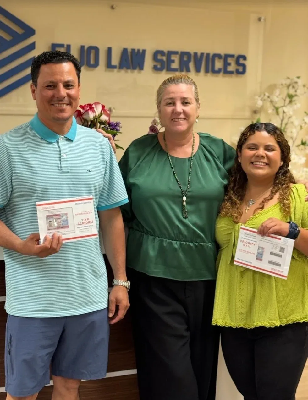 Maria Eijo stands with a man and a woman, each holding a document in a Priority Mail envelope, in the office lobby.