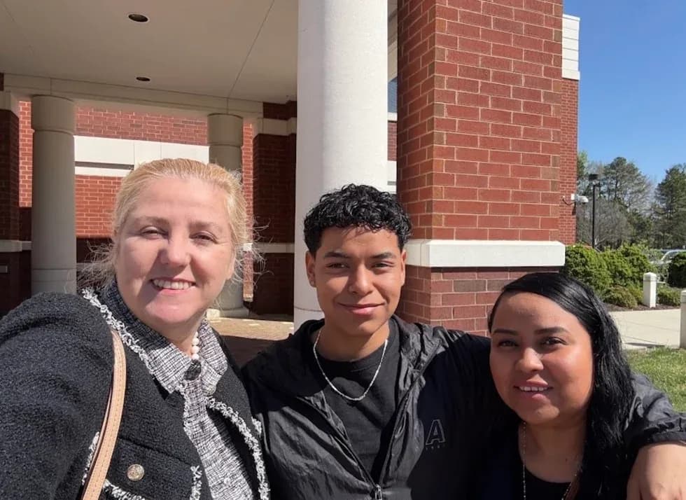 Maria Eijo stands with a young man and a woman outside a brick building with white columns.