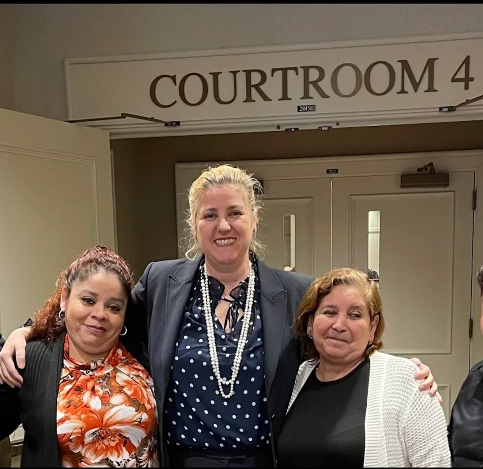 Maria Eijo stands with two women in front of a doorway marked "Courtroom 4."