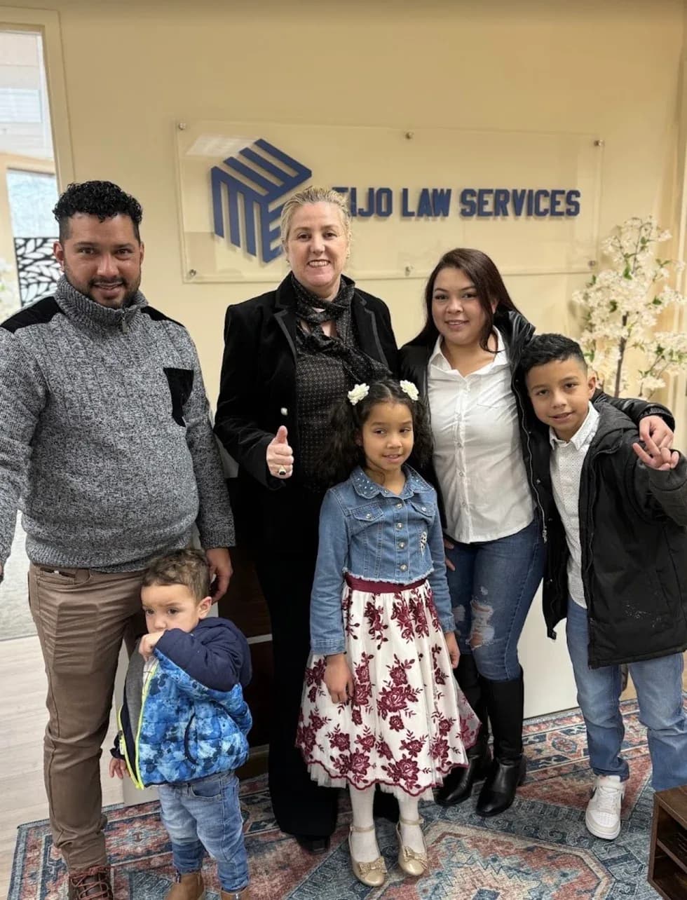 Maria Eijo stands with a family of six, including three children, in the office lobby in front of the firm’s sign.