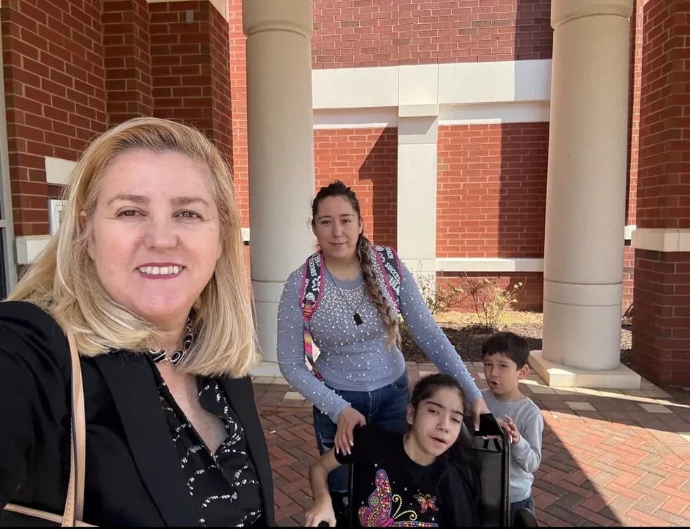 Maria Eijo poses with a woman, a boy, and a girl in a wheelchair, outside a brick building with columns.