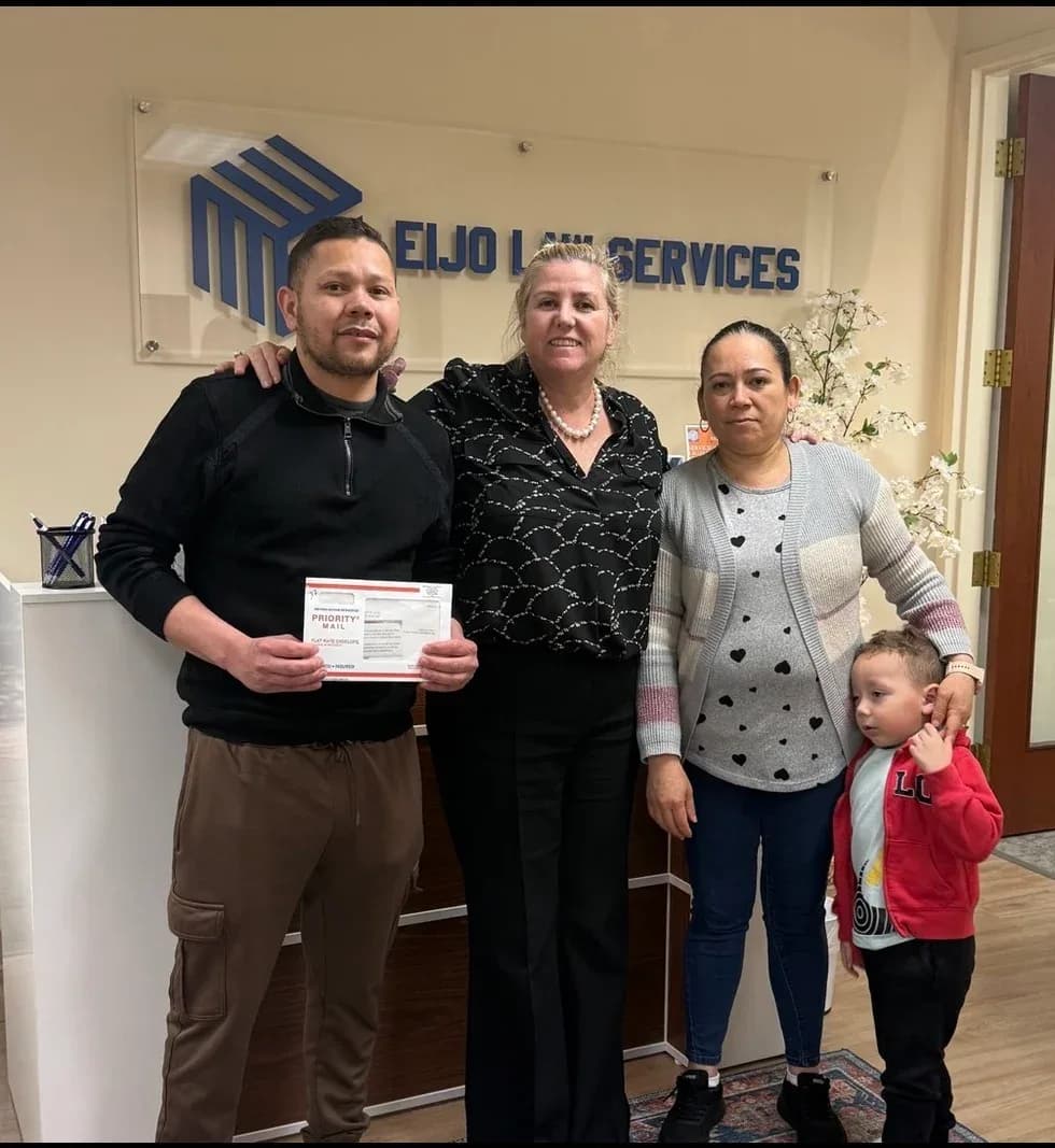 Maria Eijo stands with a man holding a Priority Mail envelope, a woman, and a young boy, in the office lobby.