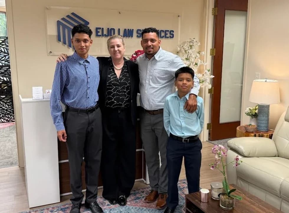 Maria Eijo stands with a father and his two sons in the office lobby, in front of the firm’s sign.