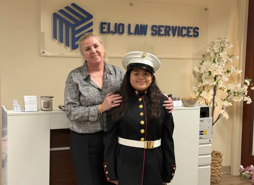 Maria Eijo stands with a young woman wearing a U.S. Marine Corps dress uniform, in front of the firm’s sign.