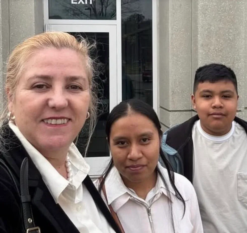 Maria Eijo stands outside an office building with a woman and a young boy, near an exit door.