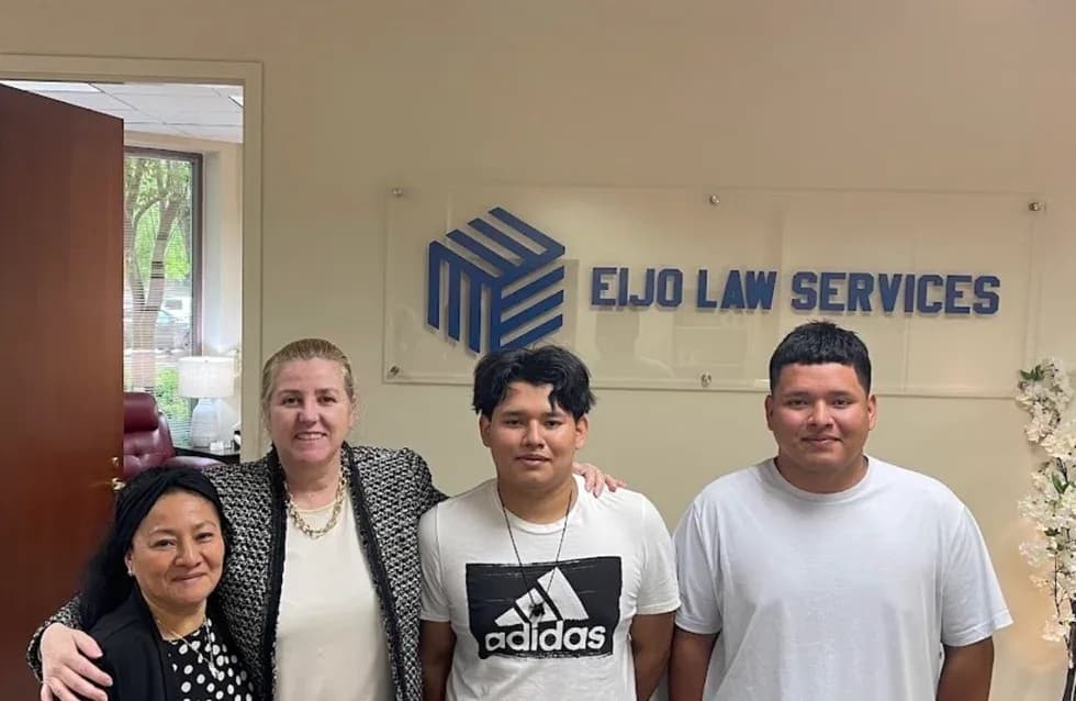 Two men and two women stand together in the Eijo Law Services reception area, in front of the firm’s wall sign.