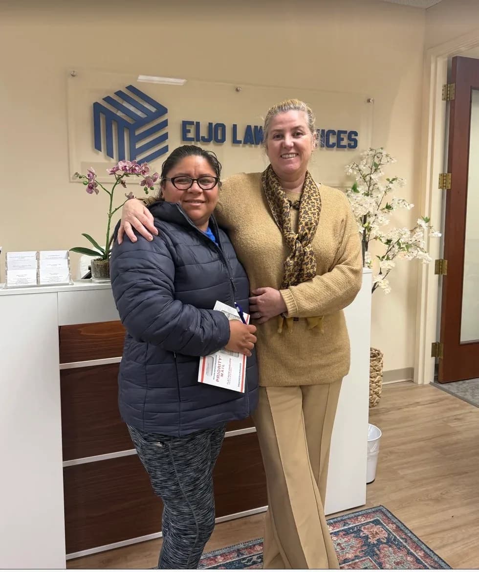 Two women embrace in the office lobby; one is holding a Priority Mail envelope.