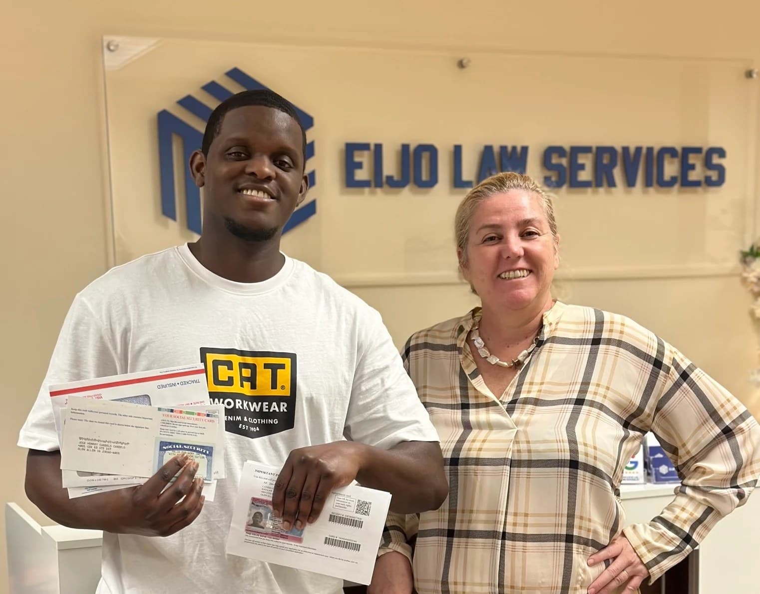 Un cliente sostiene sus documentos migratorios aprobados junto a la abogada Maria Eijo de Tezanos Pinto frente al rótulo de la oficina de Eijo Law Services