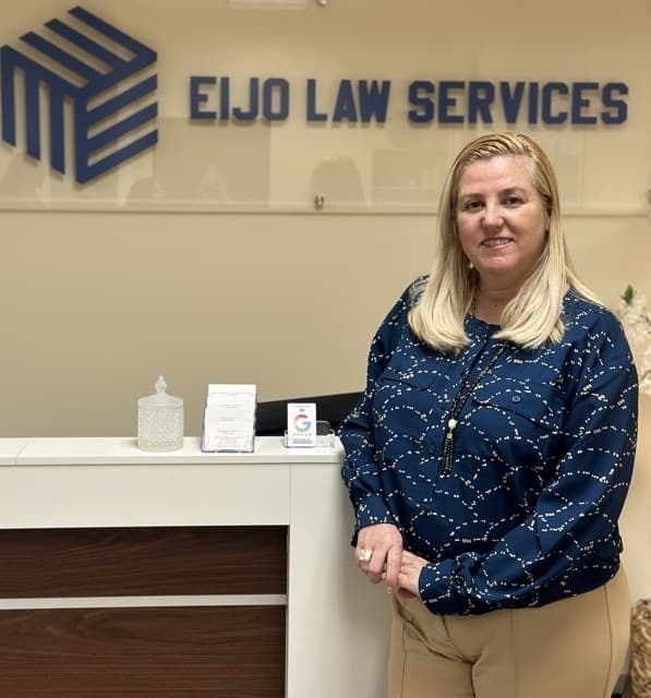 La abogada Maria Eijo de Tezanos Pinto de pie en el mostrador de recepción de Eijo Law Services, bajo el rótulo con el logotipo de la firma